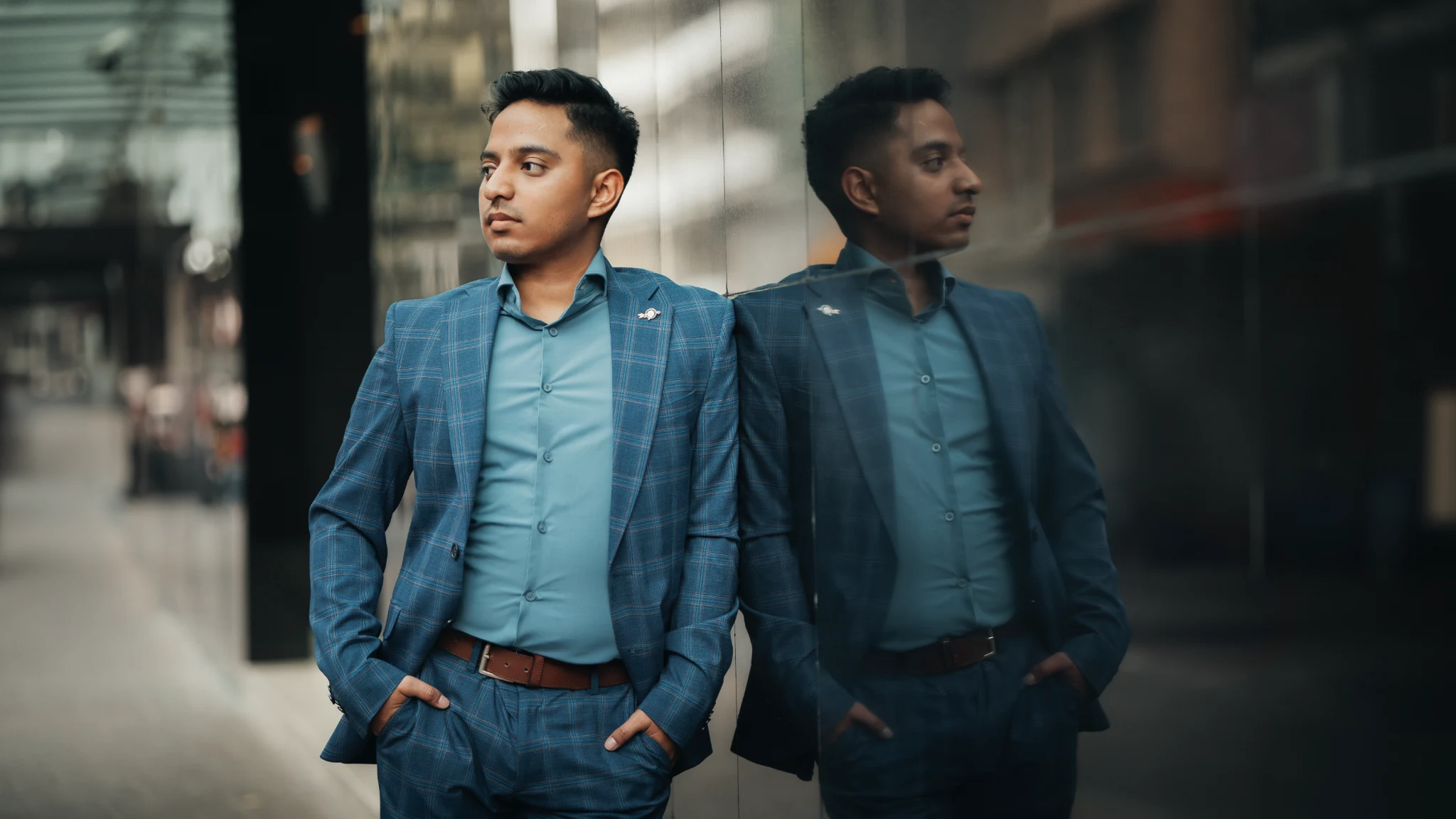 Luis González con traje azul, apoyado junto a una pared de cristal que refleja su figura